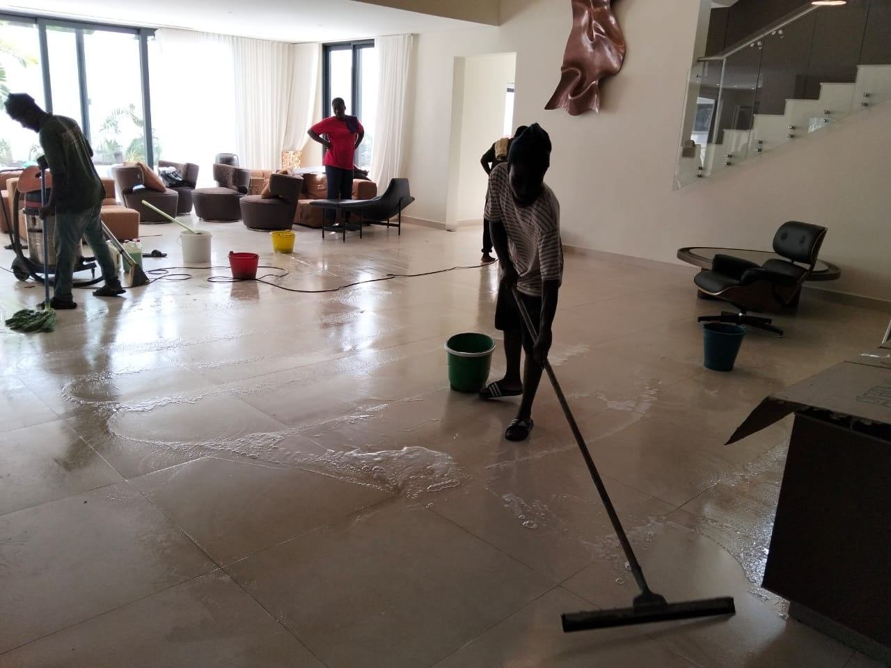 Dromo Cleaning team scrubbing and squeegeeing the tiled floor of a large living room in Accra