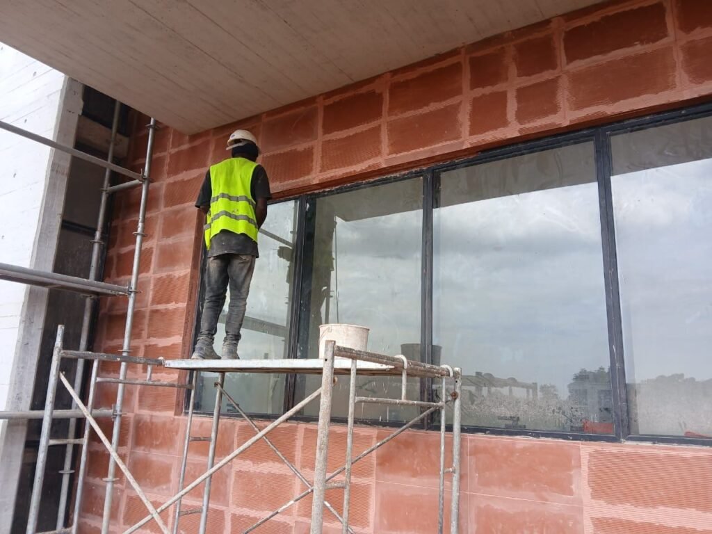 Cleaner in a safety vest cleaning large windows from scaffolding on a new building in Accra