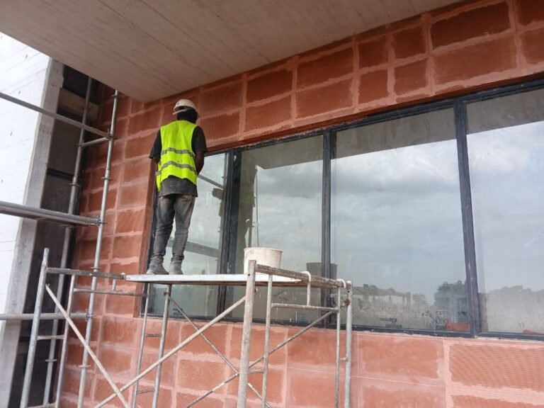 Cleaner in a safety vest cleaning large windows from scaffolding on a new building in Accra